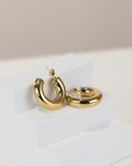 Gold hoop huggie earrings on a white stand