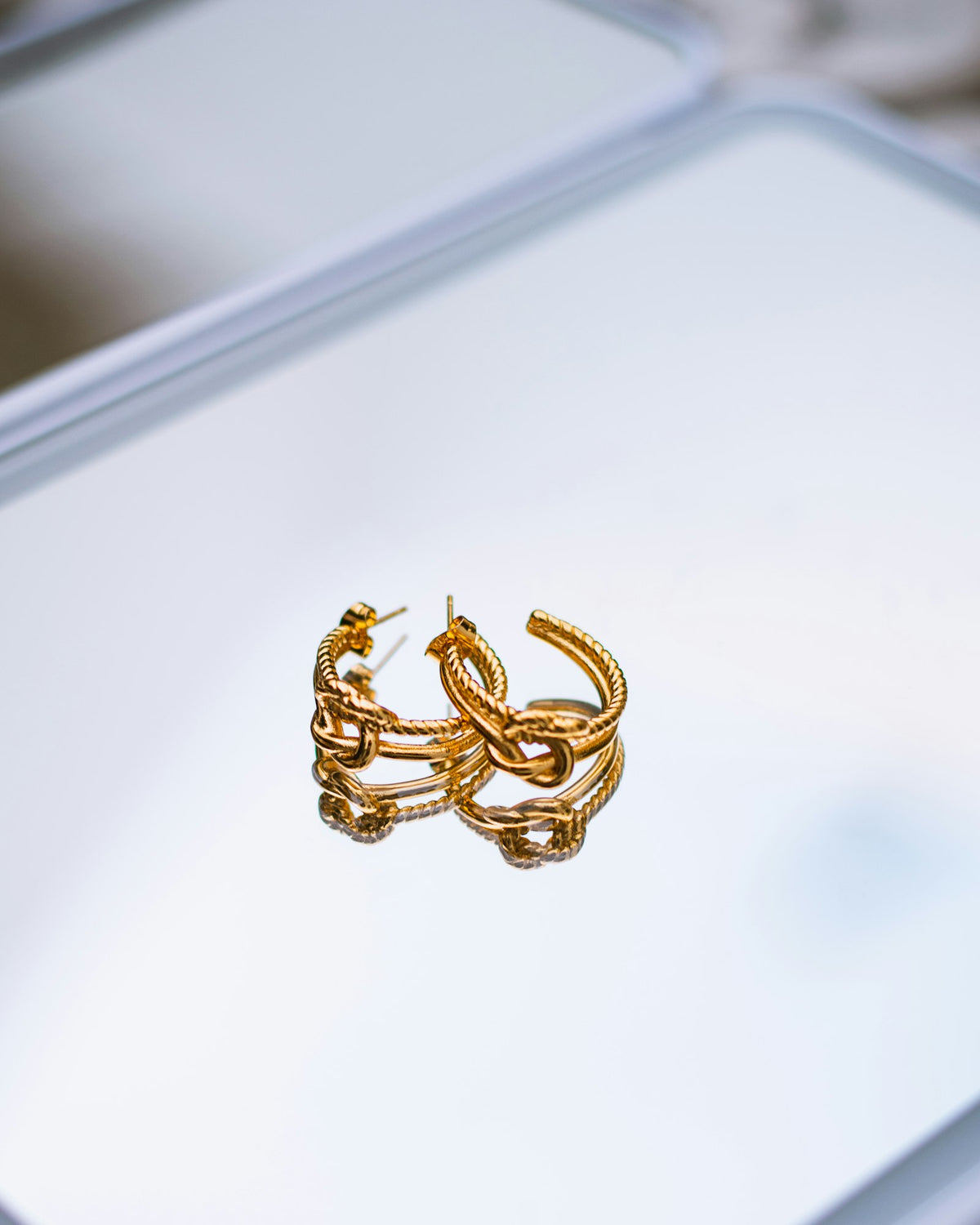 Gold chain-link hoop earrings on a mirror