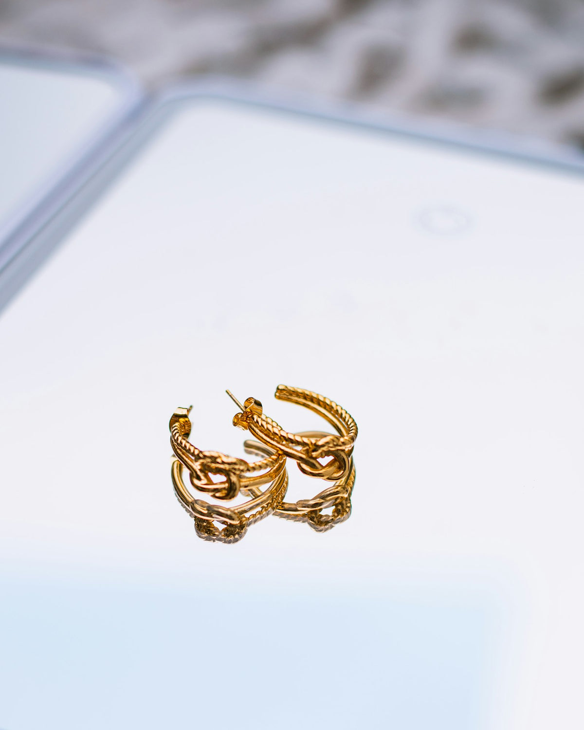Gold chain-link hoop earrings on a reflective surface