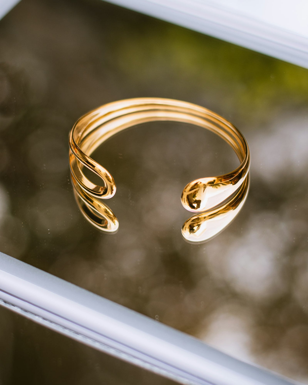 Gold open cuff bracelet on a reflective surface